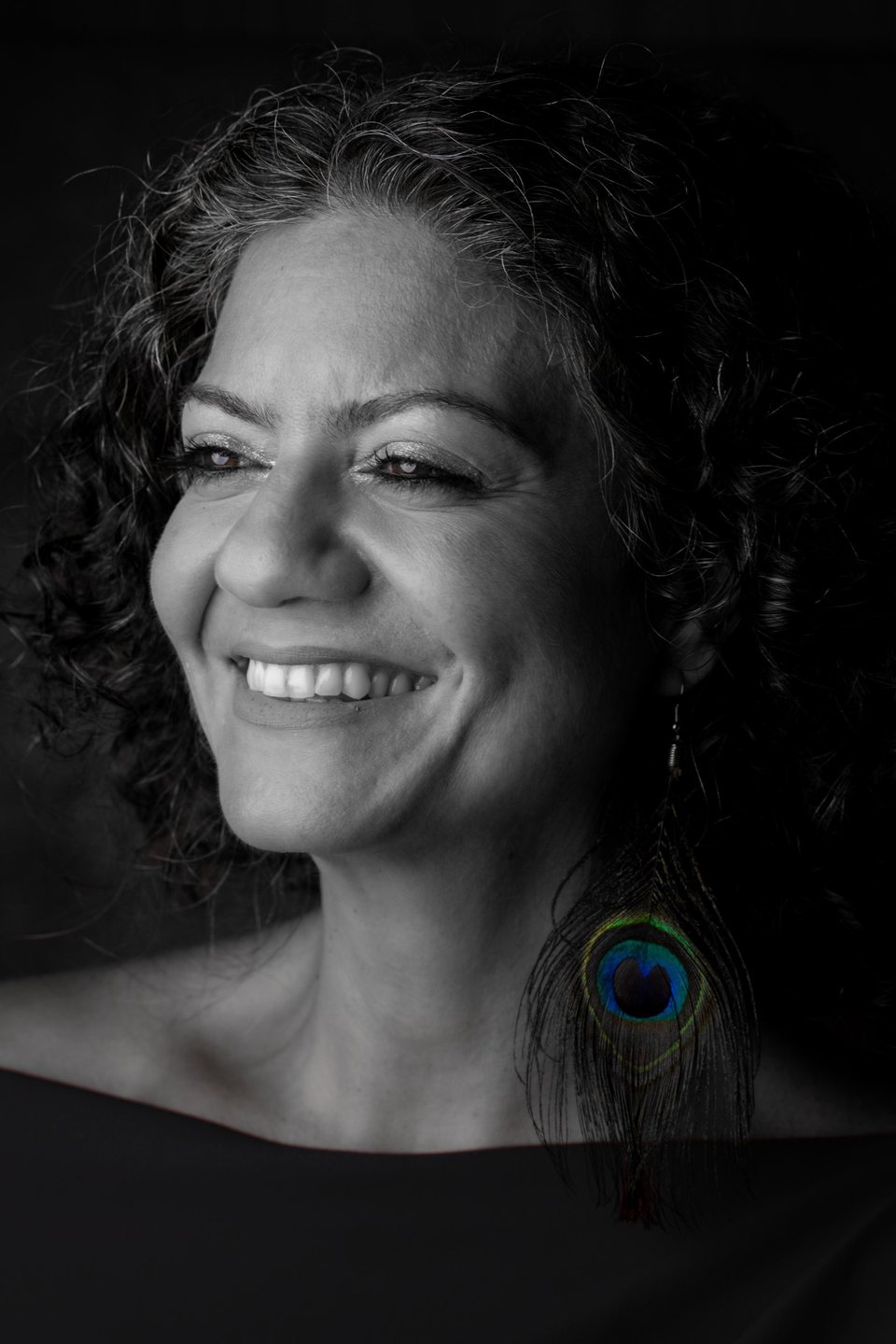 Rouba Zeidan smiling, black and white portrait with a peacock feather earring